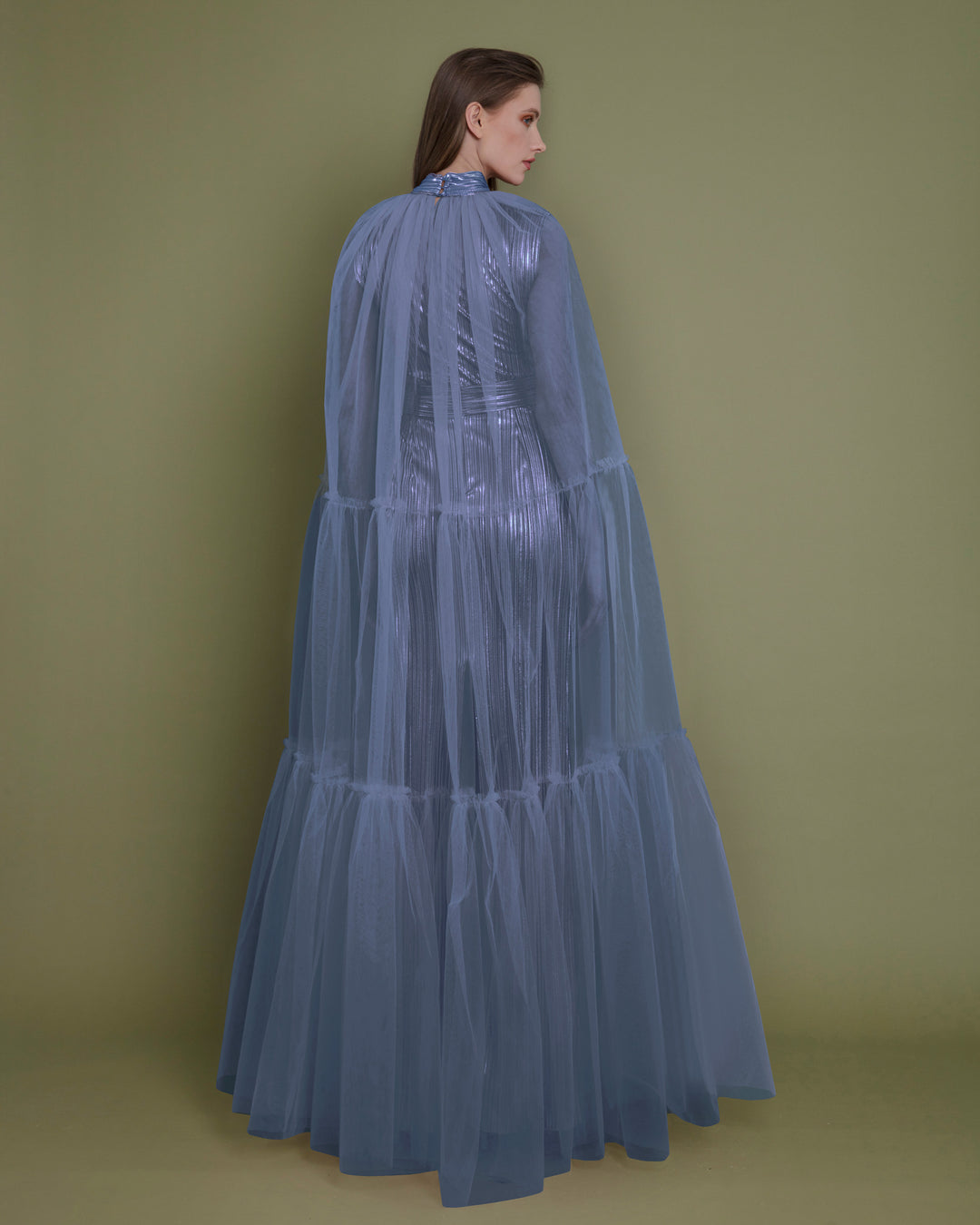 The back of a slim cut metallic blue evening dress in pleated fabric, paired with a tulle ruffled cape.