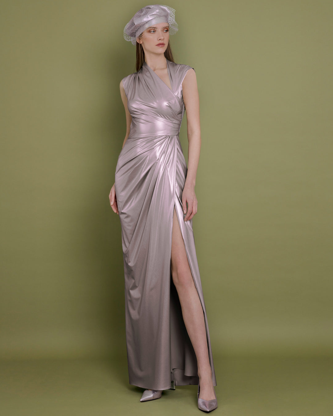 The back of an asymmetrical neckline evening dress in metallic pink latex fabric, with draping details on the waist and a side slit.