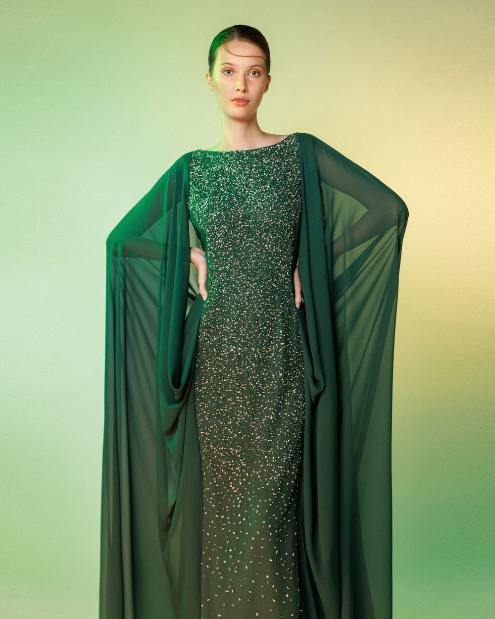 A straight-cut fully beaded long evening dress with a chiffon cape like sleeves, attached to the back making some draping.