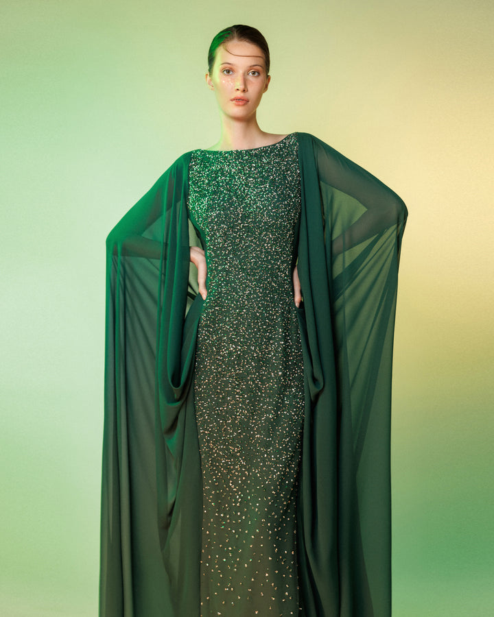 A straight-cut fully beaded long evening dress with a chiffon cape like sleeves, attached to the back making some draping.