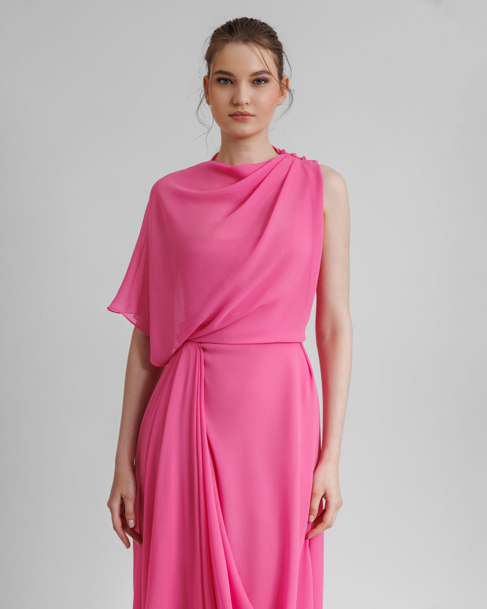 A close-up of an asymmetrical pink chiffon evening dress with draping details featuring a slit on the side.