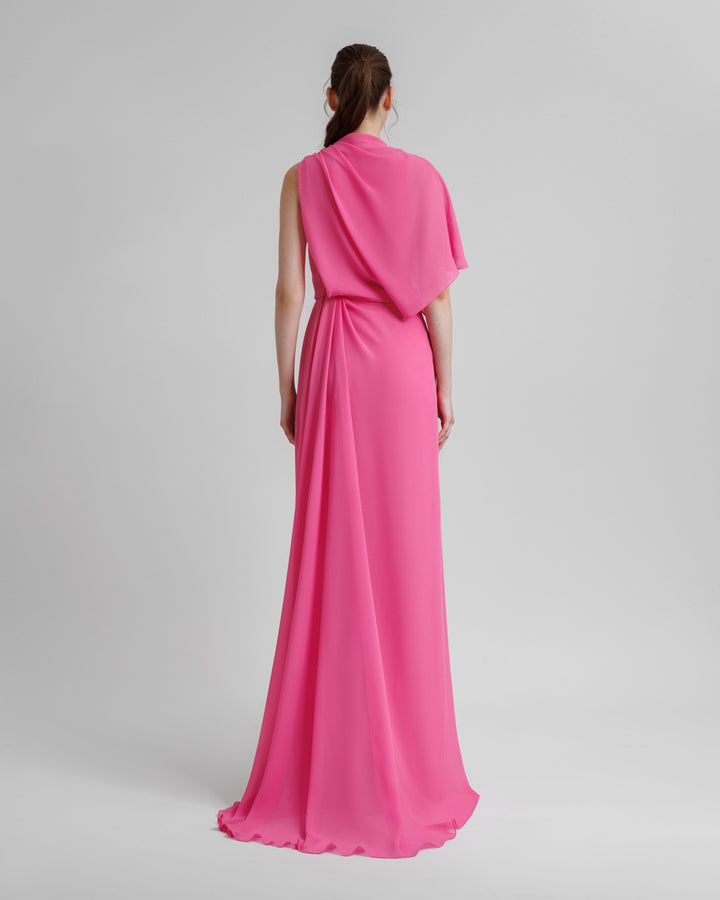 The back of an asymmetrical pink chiffon evening dress with draping details featuring a slit on the side.