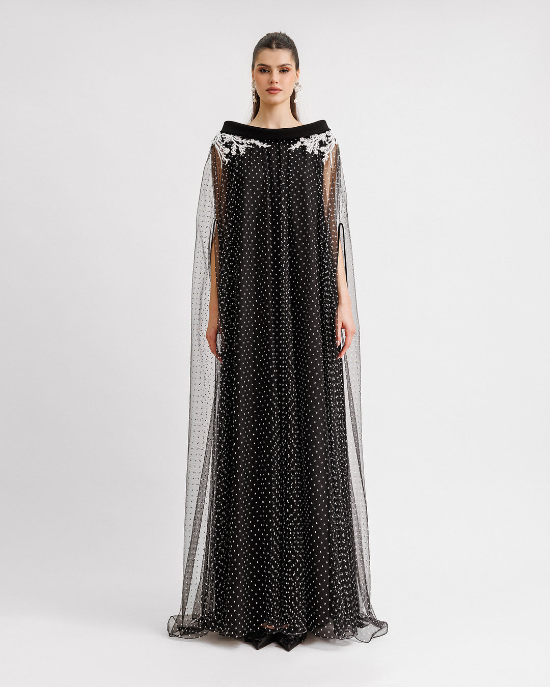 A kaftan-style black dress with a crepe fold-over at the neckline and white beading details on the shoulders.