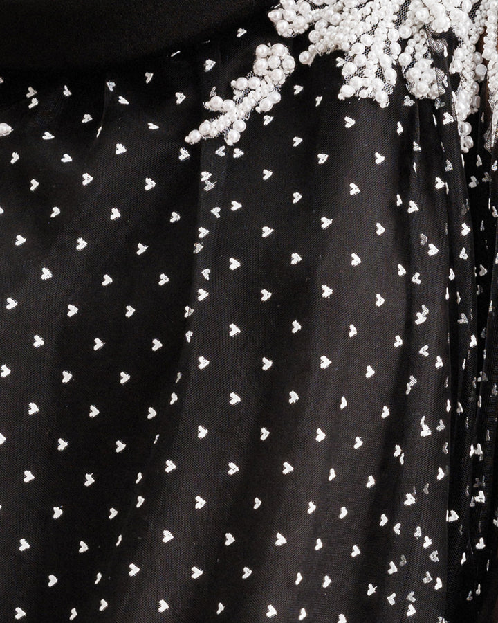 A close-up of a black tulle fabric with mini white hearts and beading.