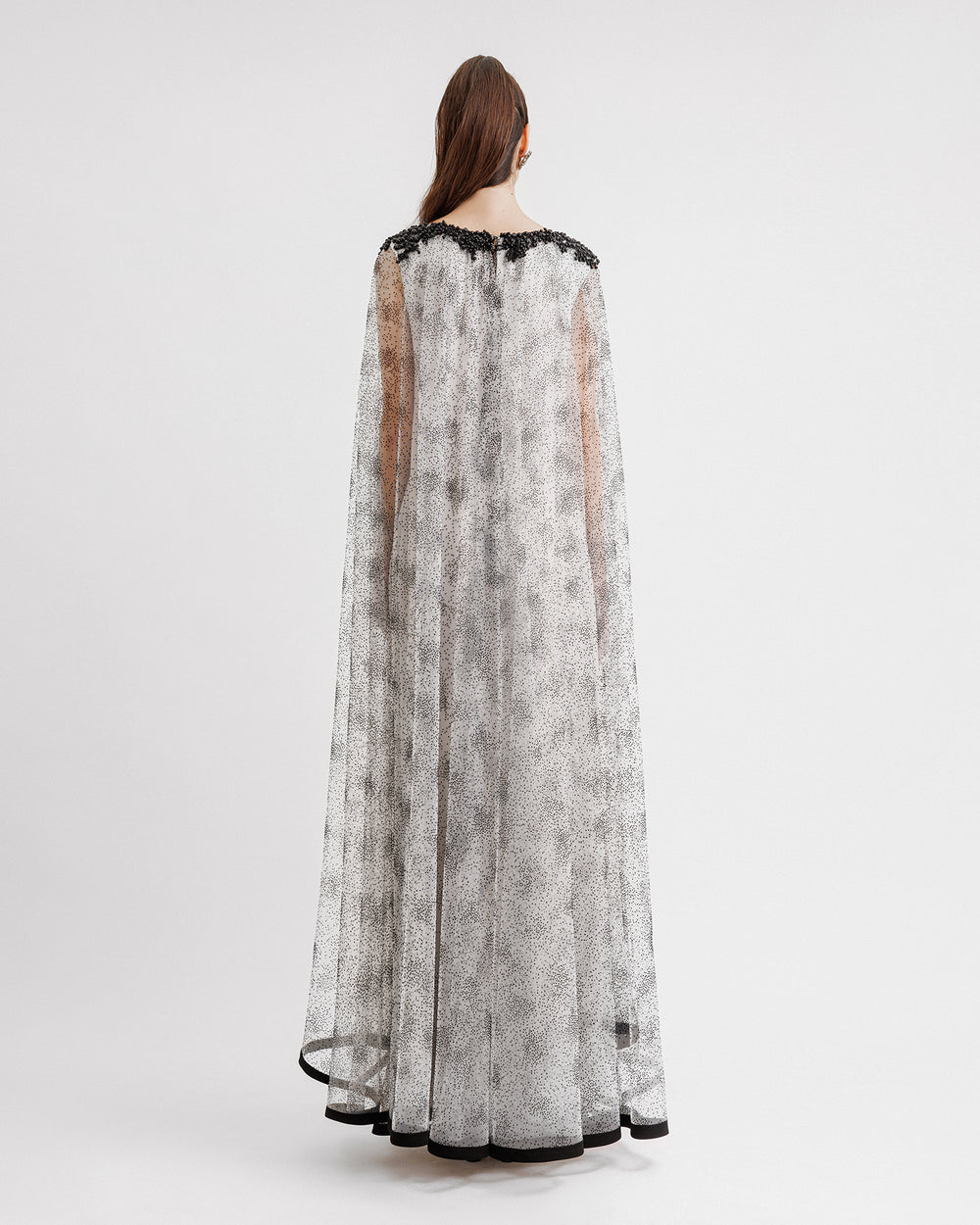 The back of a loose-cut kaftan-style black dotted white tulle dress featuring beadings on the neckline and a black hemline.