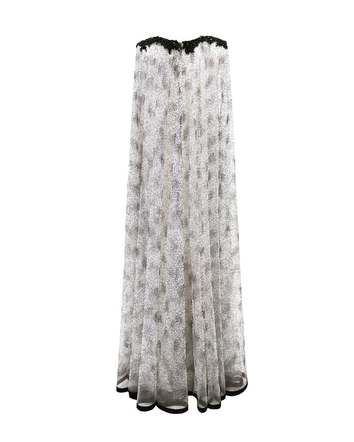 The back of a loose-cut kaftan-style black dotted white tulle dress featuring beadings on the neckline and a black hemline.