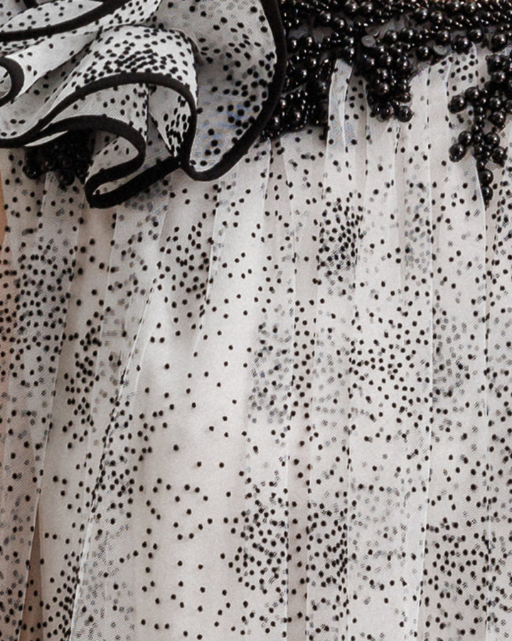 A close-up of  a black dotted white tulle fabric with beading details and a draped flower.