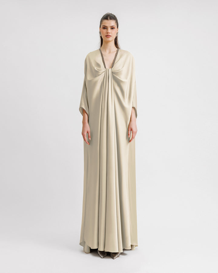 A kaftan-style evening dress with a draped beaded neckline, featuring three-quarters sleeves with beaded cuffs.