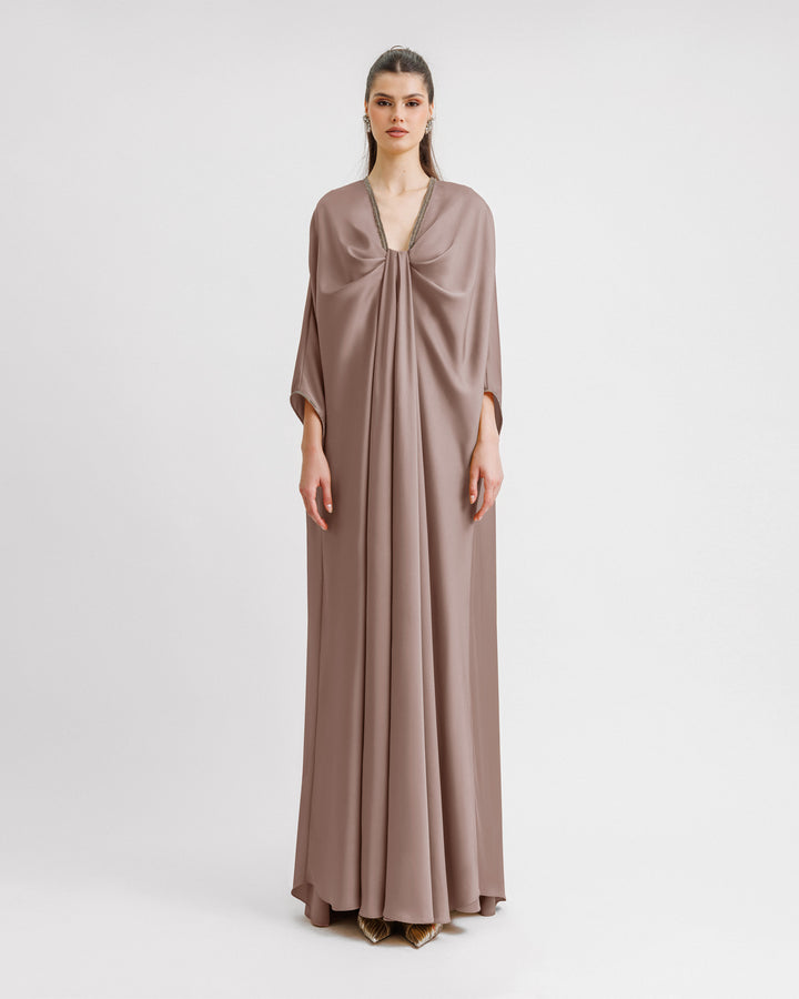 A kaftan-style evening dress in taupe color with a draped beaded neckline, featuring three-quarters sleeves.