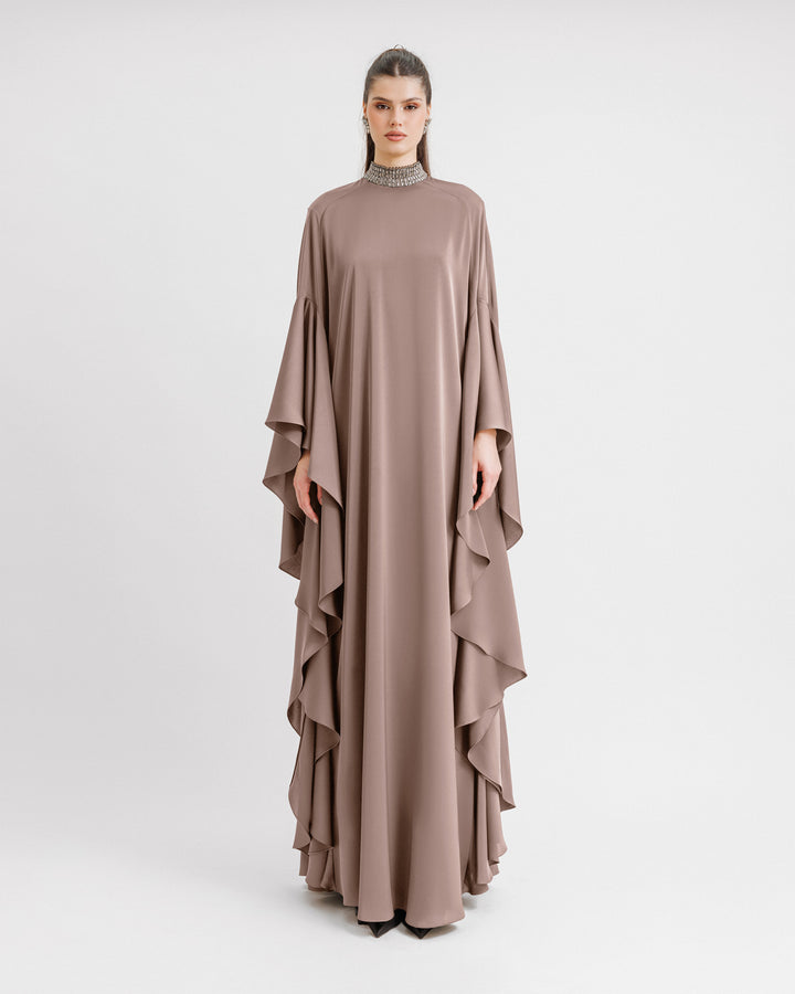 A kaftan-style evening dress in taupe color with a beaded collar and ruffled floor-length sleeves.