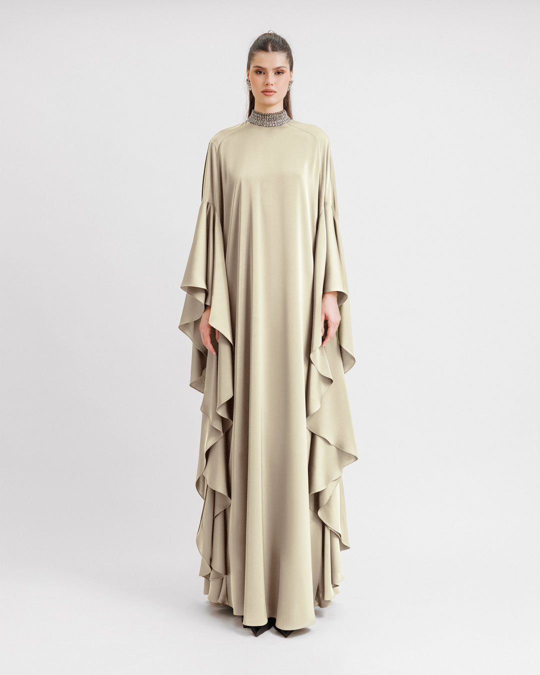 A kaftan-style evening dress in cream color satin with a beaded collar and ruffled floor-length sleeves.