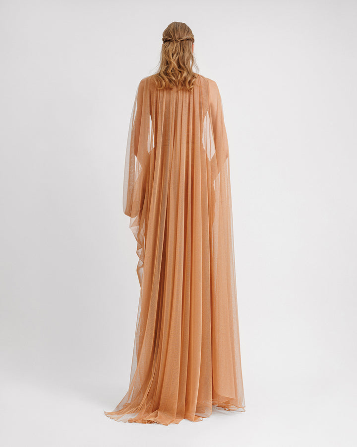 The back of a draped shiny tulle evening dress in copper color with asymmetrical cape-like sleeves.