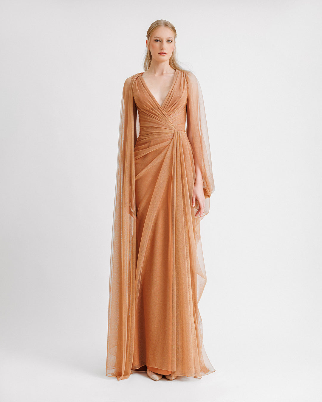 A V-neckline draped shiny tulle evening dress in copper color with asymmetrical cape-like sleeves.