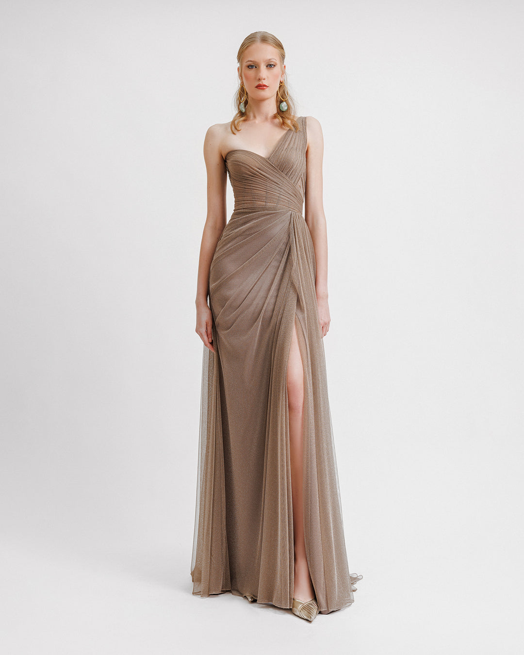 A one-shoulder draped shiny tulle dress in taupe color featuring a slit on the side.