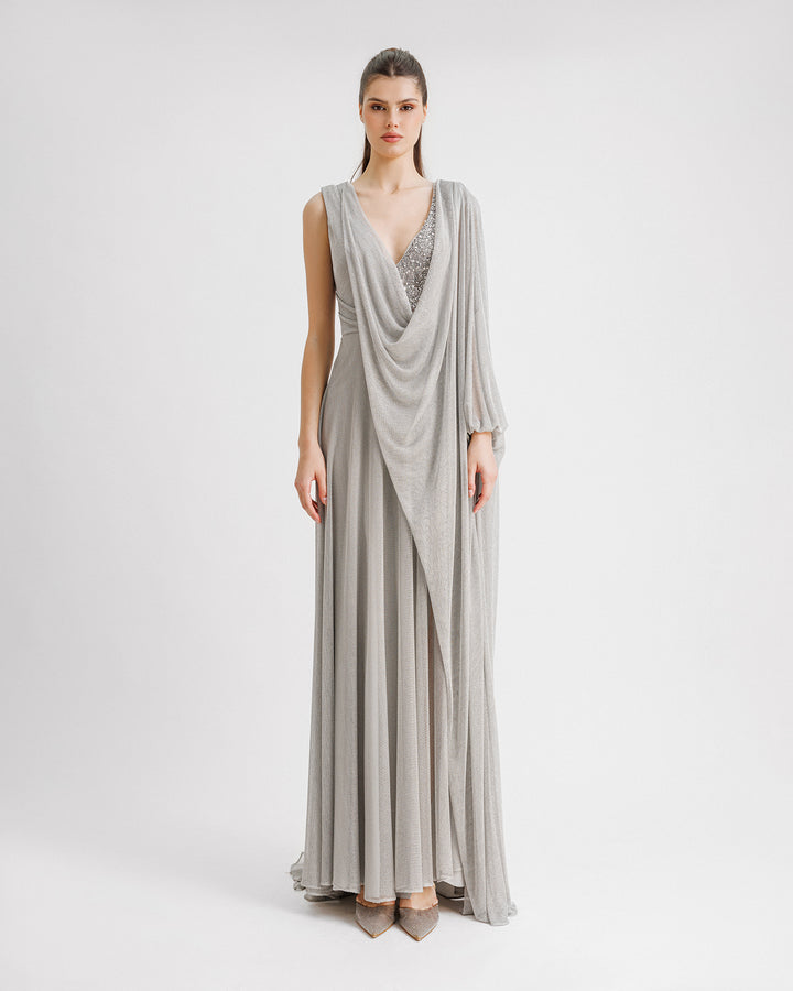 A V-neckline silver evening dress in net tulle with beading details on the side and a long draped cape-like one sleeve.