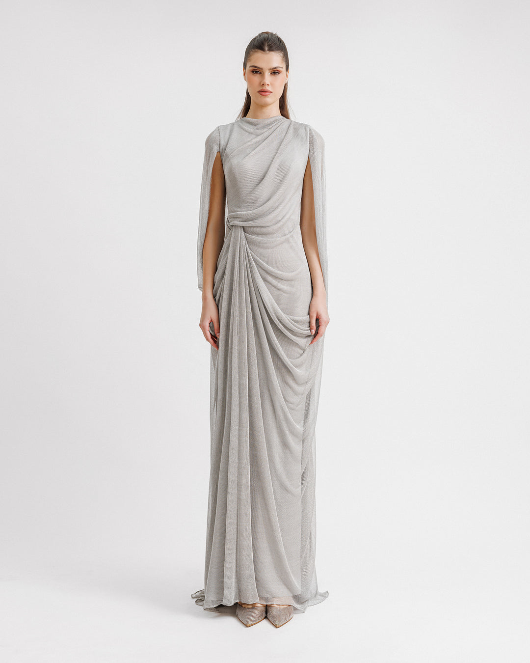 A long silver net tulle evening dress with draping on the neckline and waist, and cape-like sleeves.