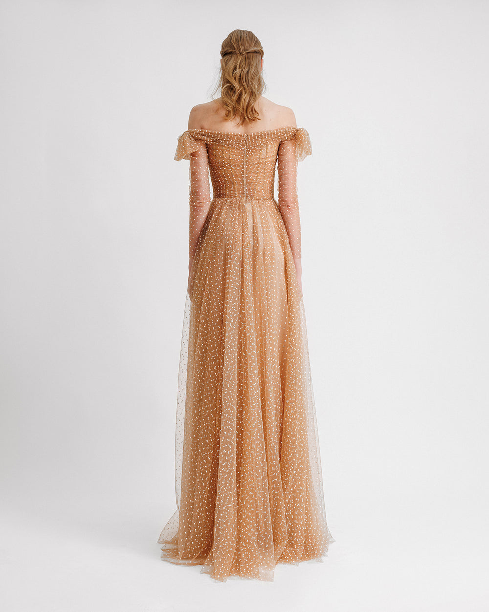 The back of an off-the-shoulders evening dress in white heart pattern caramel tulle with a draped neckline and see-through sleeves.