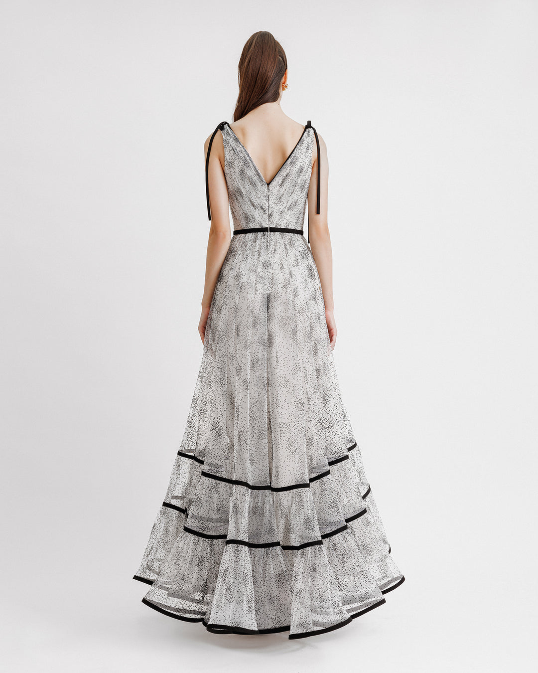 The back of a black dotted white tulle evening dress with a flowy structured skirt and a V-shaped open back.