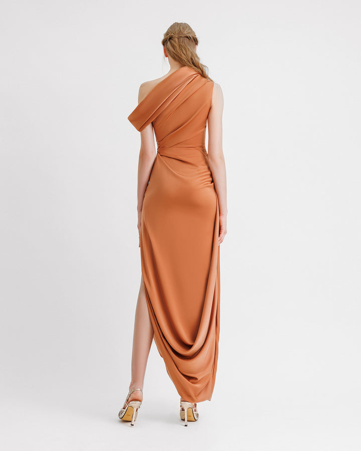 The back of a draped copper evening dress in satin fabric featuring an asymmetrical neckline and hemline, and a slit on the side.