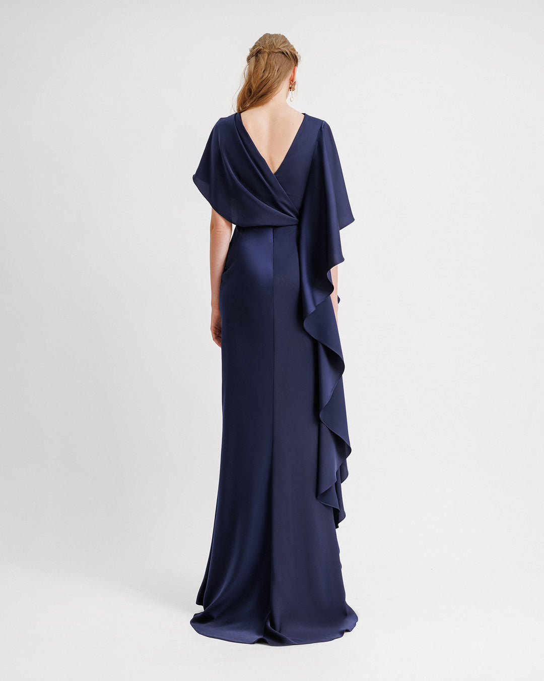 The back of an asymmetrical draped navy evening dress with a ruffled sleeve going all the way down to the hemline, and a V-shaped open back.