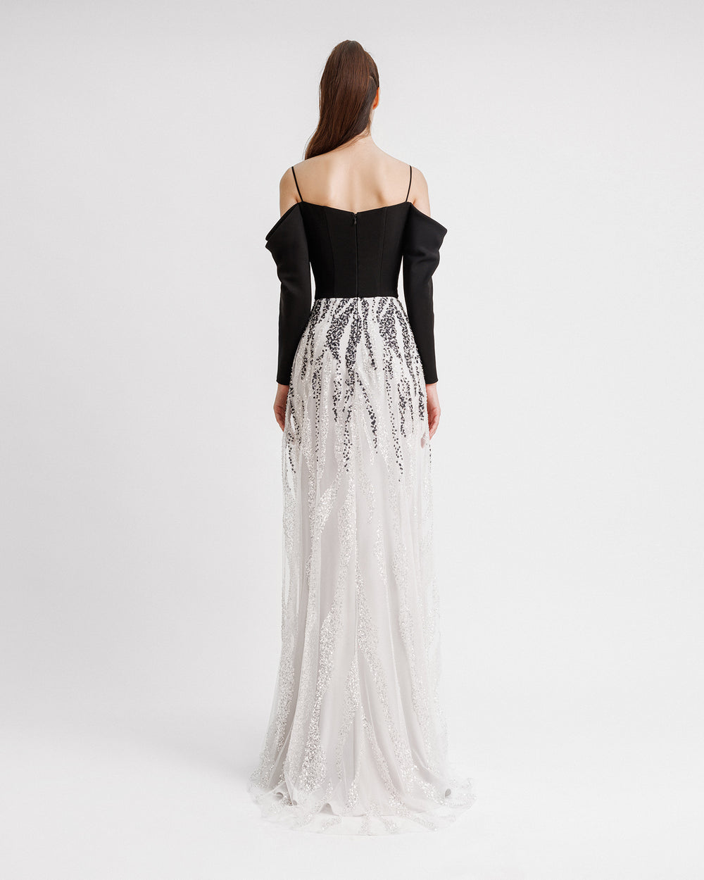 The back of a long black and white evening dress with draped off-the-shoulder sleeves in black crepe fabric and a black and white sequins overlaying a long white skirt.