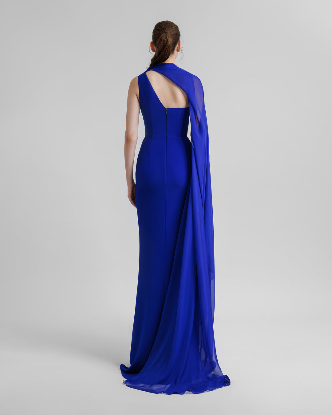 The back of an asymmetrical floor length shawl collar blue evening dress.