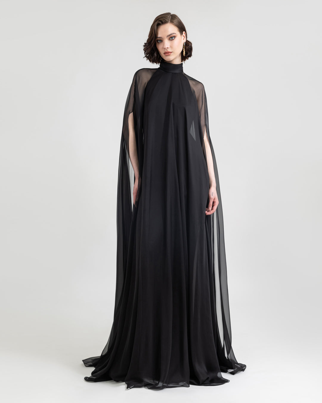 A slim cut crepe long black evening dress with see through overlayered cape.