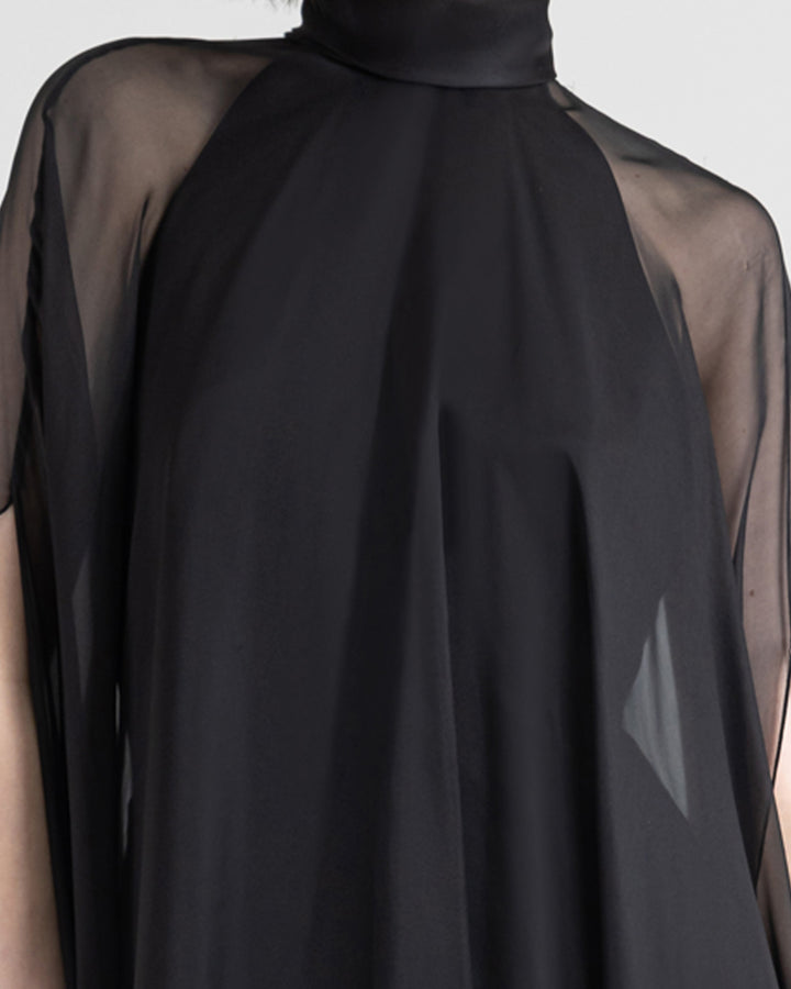 A close-up of a slim cut crepe long black evening dress with see through overlayered cape.