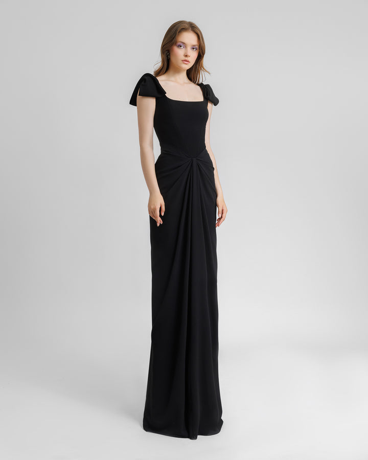 A squared neckline corset long black evening dress with bow designs on the shoulders and draping details on the waist.