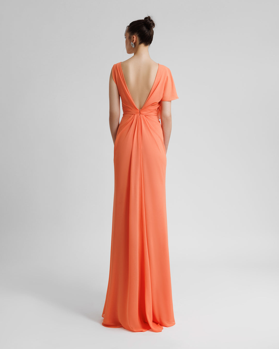 A draped long peach evening dress with asymmetrical sleeves, and an open V-shaped back.