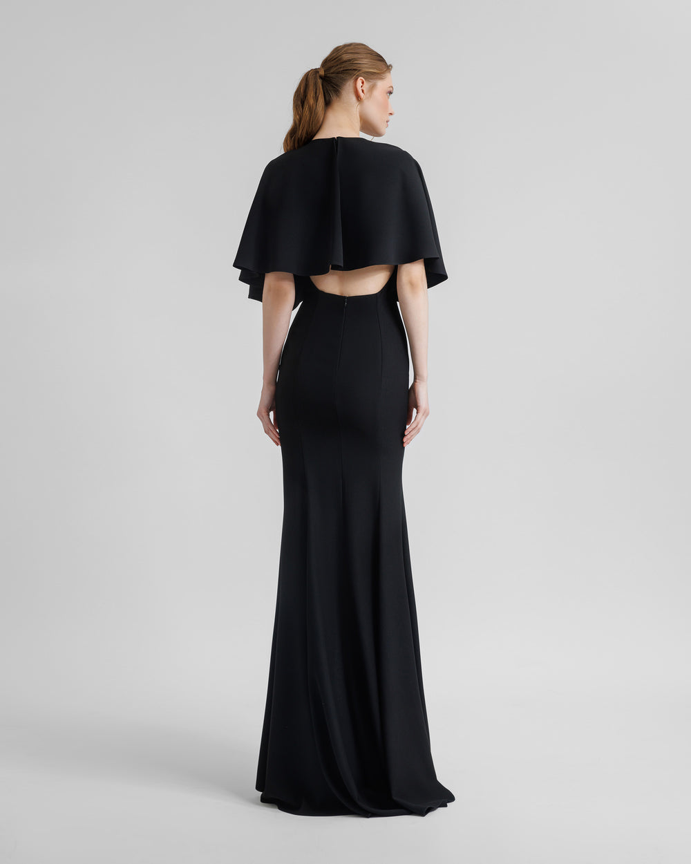 The back of a slim-cut black evening dress with a wide cape-like sleeves, and an open lower back.