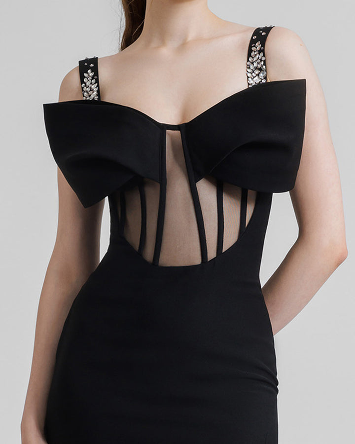 A close-up of a slim-cut black long evening dress featuring a see-through corset with a bow off-shoulders design and beaded straps.