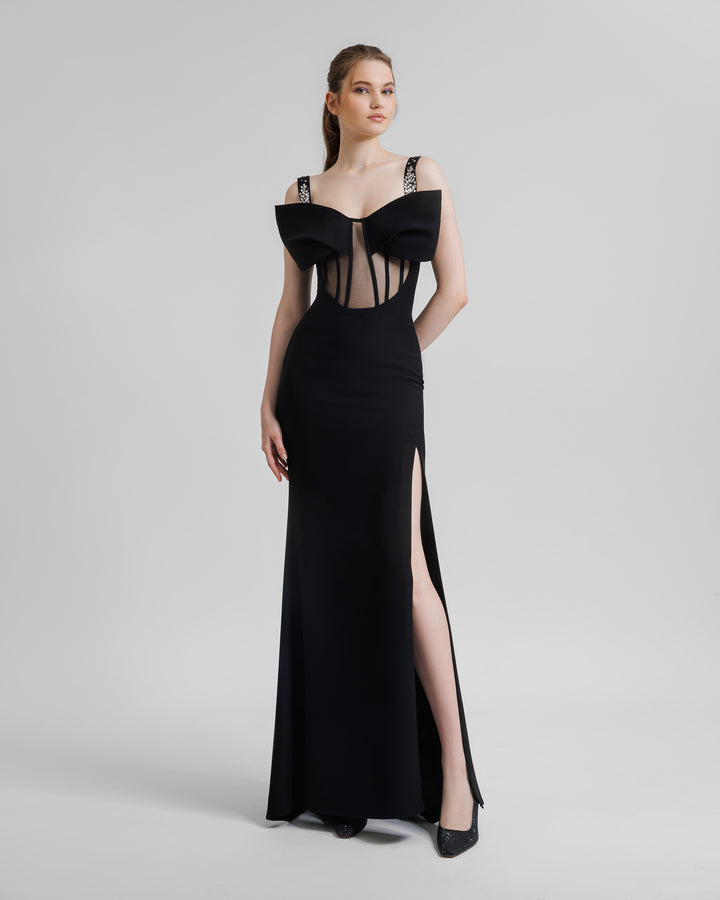 A slim-cut black long evening dress featuring a see-through corset with a bow off-shoulders design, beaded straps, and a slit on the side.