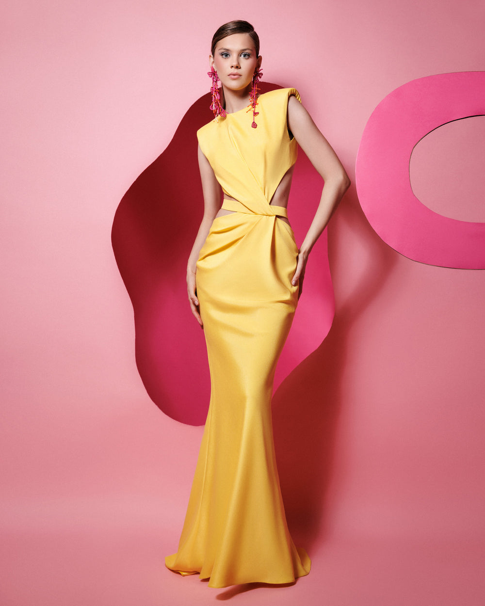 A slim-cut yellow dress featuring padded shoulders, draping and cut-outs on the waist, and an open back.