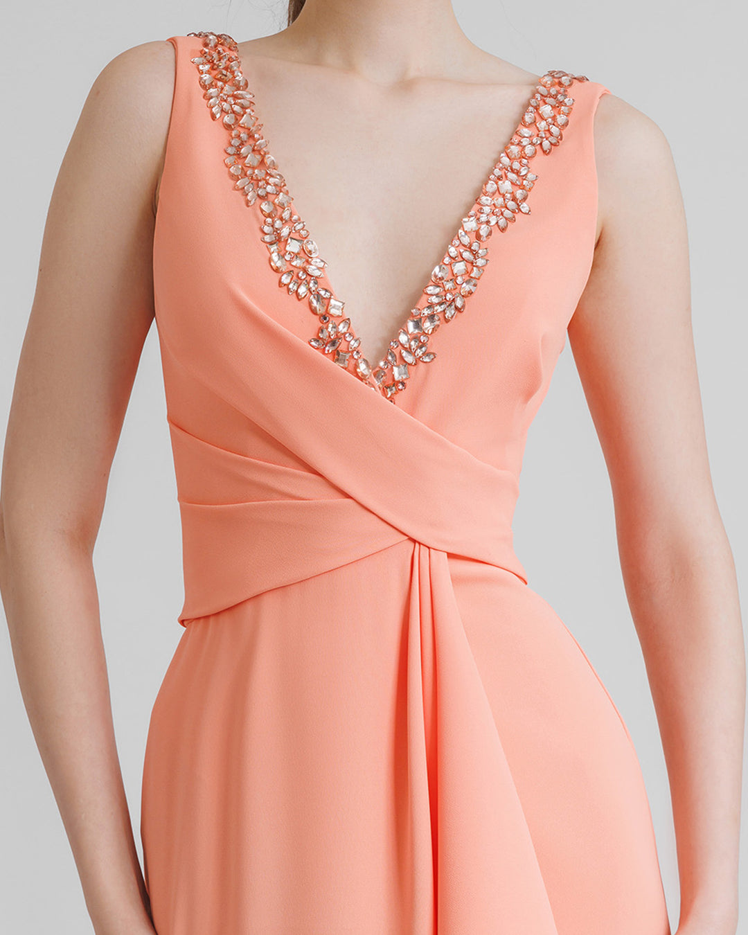 A close-up of a peach beaded V-neckline evening dress featuring draping on the waist.