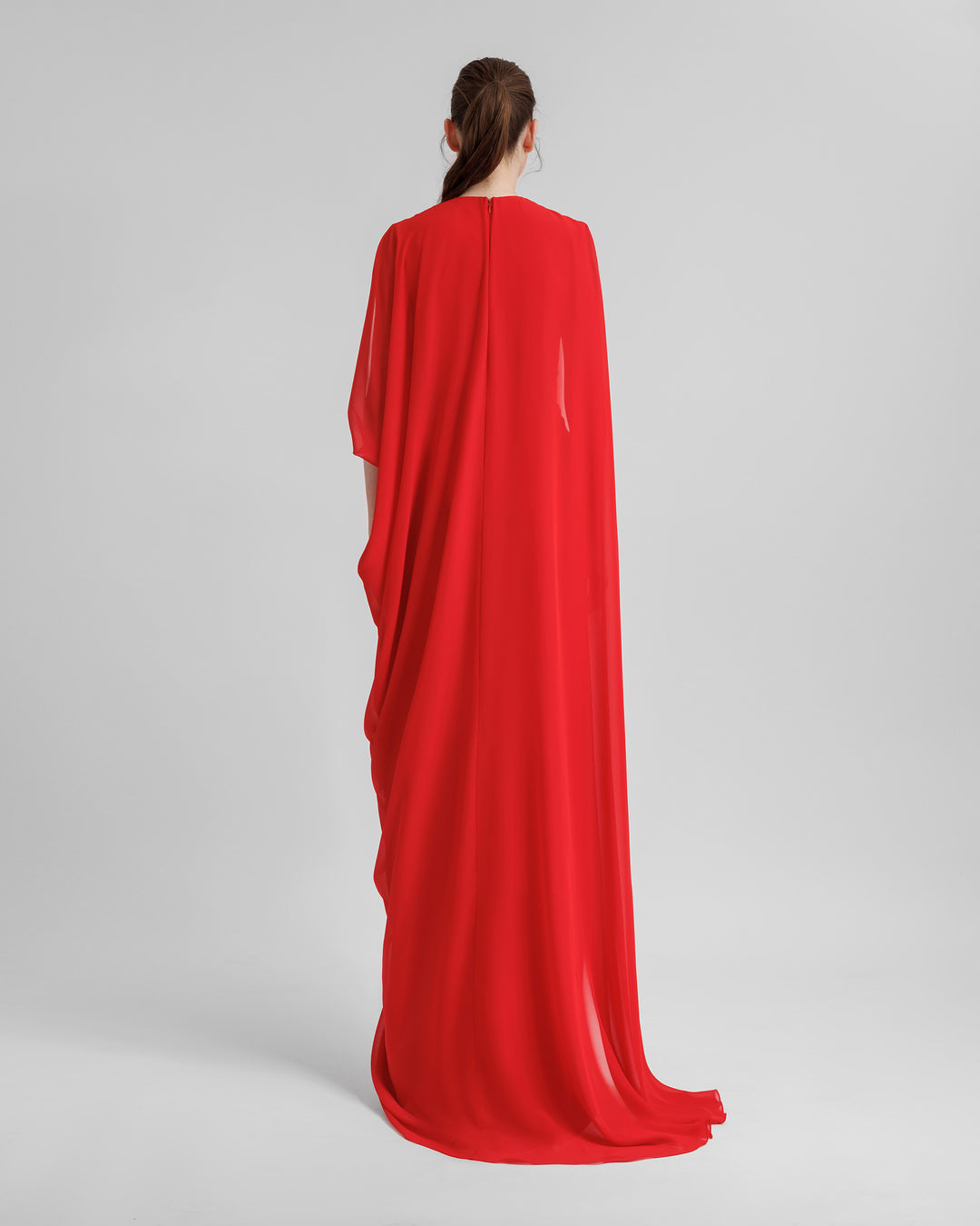 The back of an asymmetrical V-neckline, red evening dress with draping details, and a long cape-like sleeves.