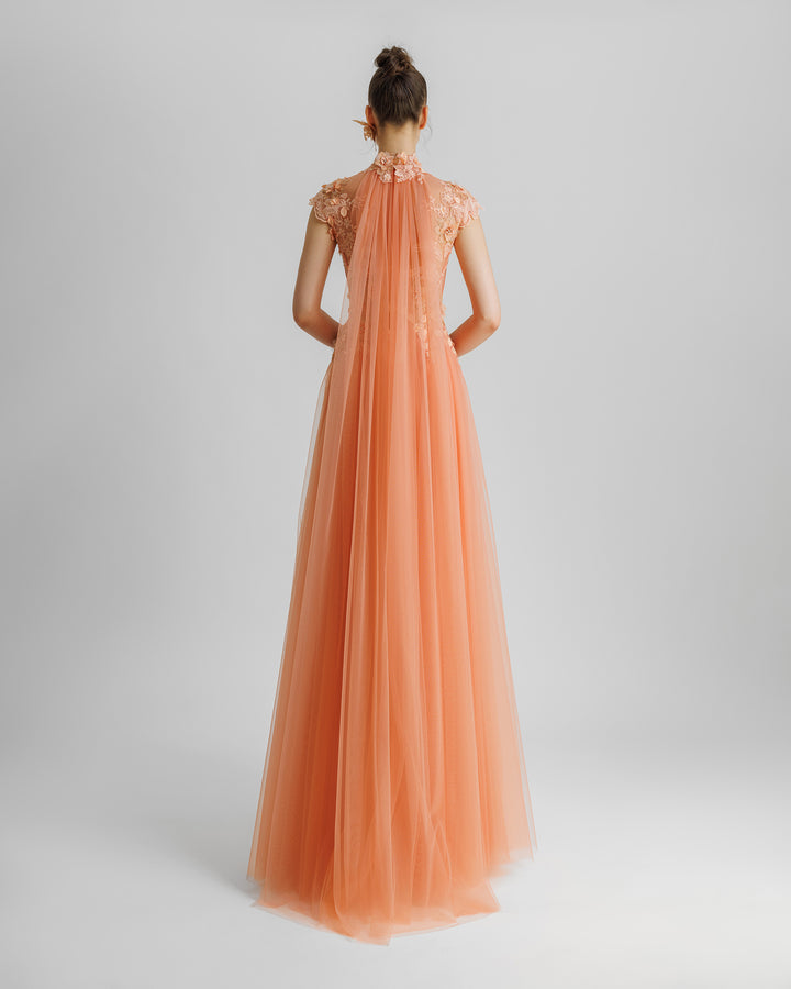 The back of a fully embellished floral see-through corset evening dress in peach color with a high-collar, tulle train going down the back neckline, and flared tulle skirt.