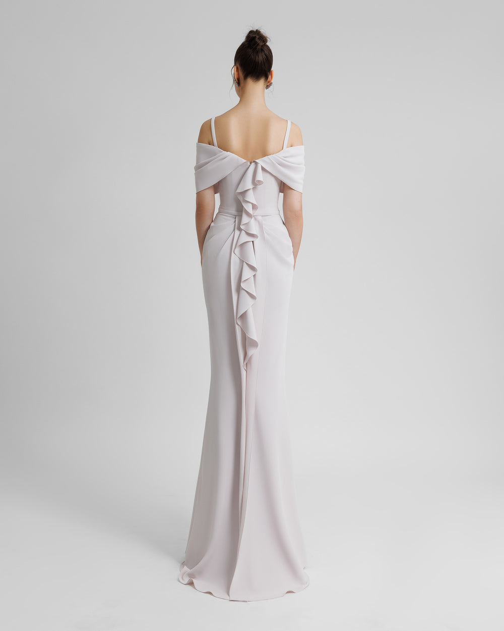 The back of a slim-cut crepe lilac evening dress with an off shoulders bow-like neckline with thin straps, a belt on the waist, and ruffles on the back.