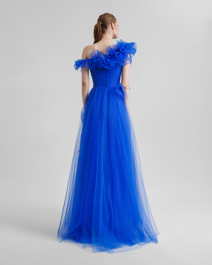 The back of a flared royal blue evening dress featuring an asymmetrical ruffled neckline, and ruffled embellishments on the skirt.