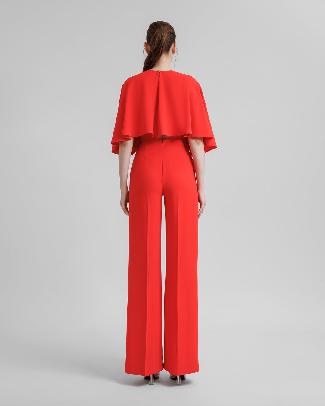 An open-back flared coral jumpsuit with wide draped cape like sleeves.