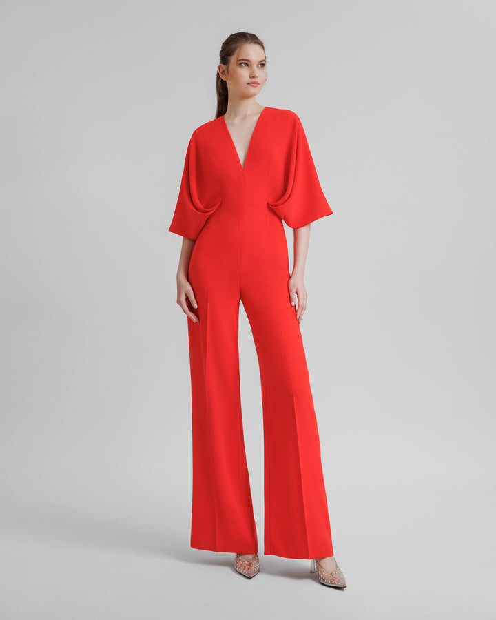 A v-neckline flared coral jumpsuit with wide draped cape like sleeves.