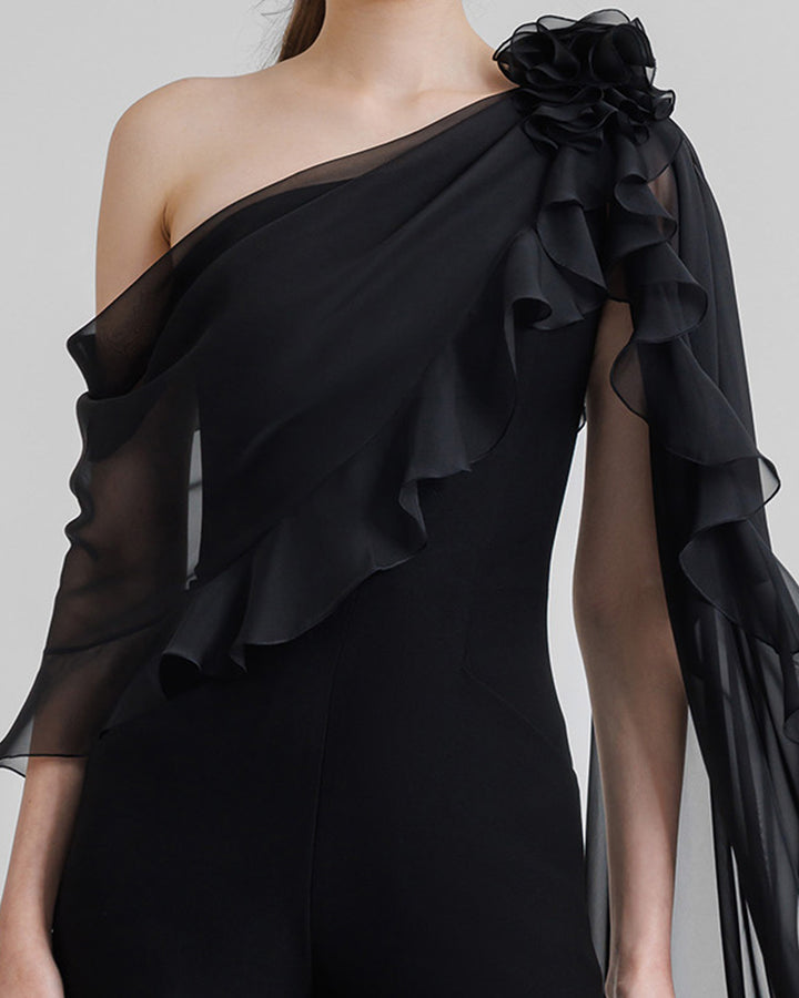 A close-up of a flared crepe black jumpsuit featuring asymmetrical ruffled cape-like chiffon sleeve with flowers details.