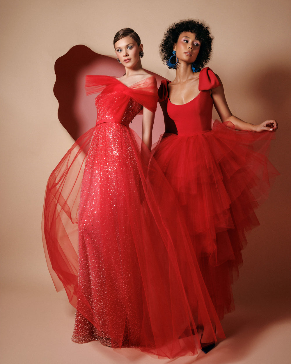 An off-the-shoulders red tulle dress with a beaded underlayer and a bow design.