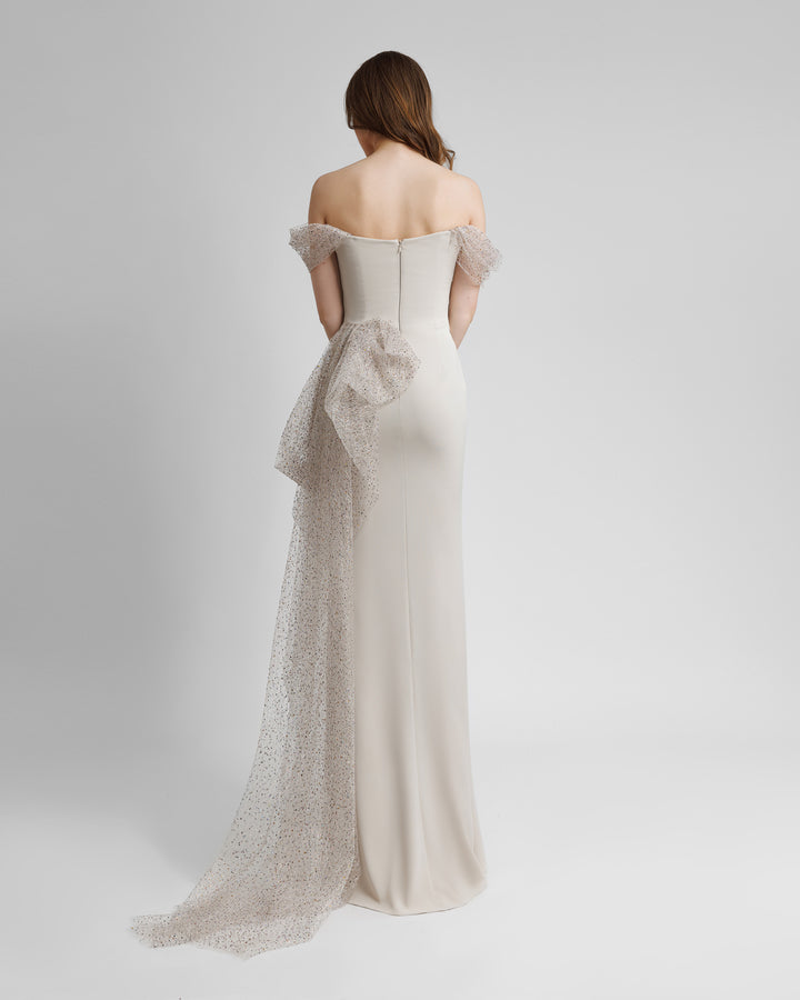 The back of an off-the-shoulders long champagne evening dress with draping details and an asymmetrical side tail.