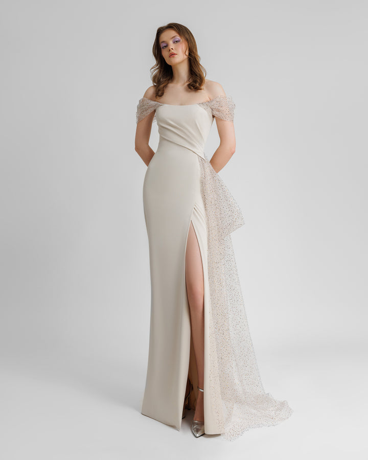 An off-the-shoulders long champagne evening dress with draping details on the bust, and an asymmetrical side tail and a slit on the side.