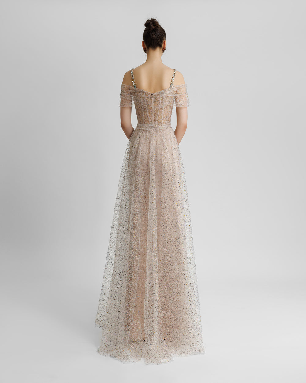 The back of an off-the-shoulders embellished corseted champagne evening dress with draping on the waist, beaded straps, and a slit on the side.