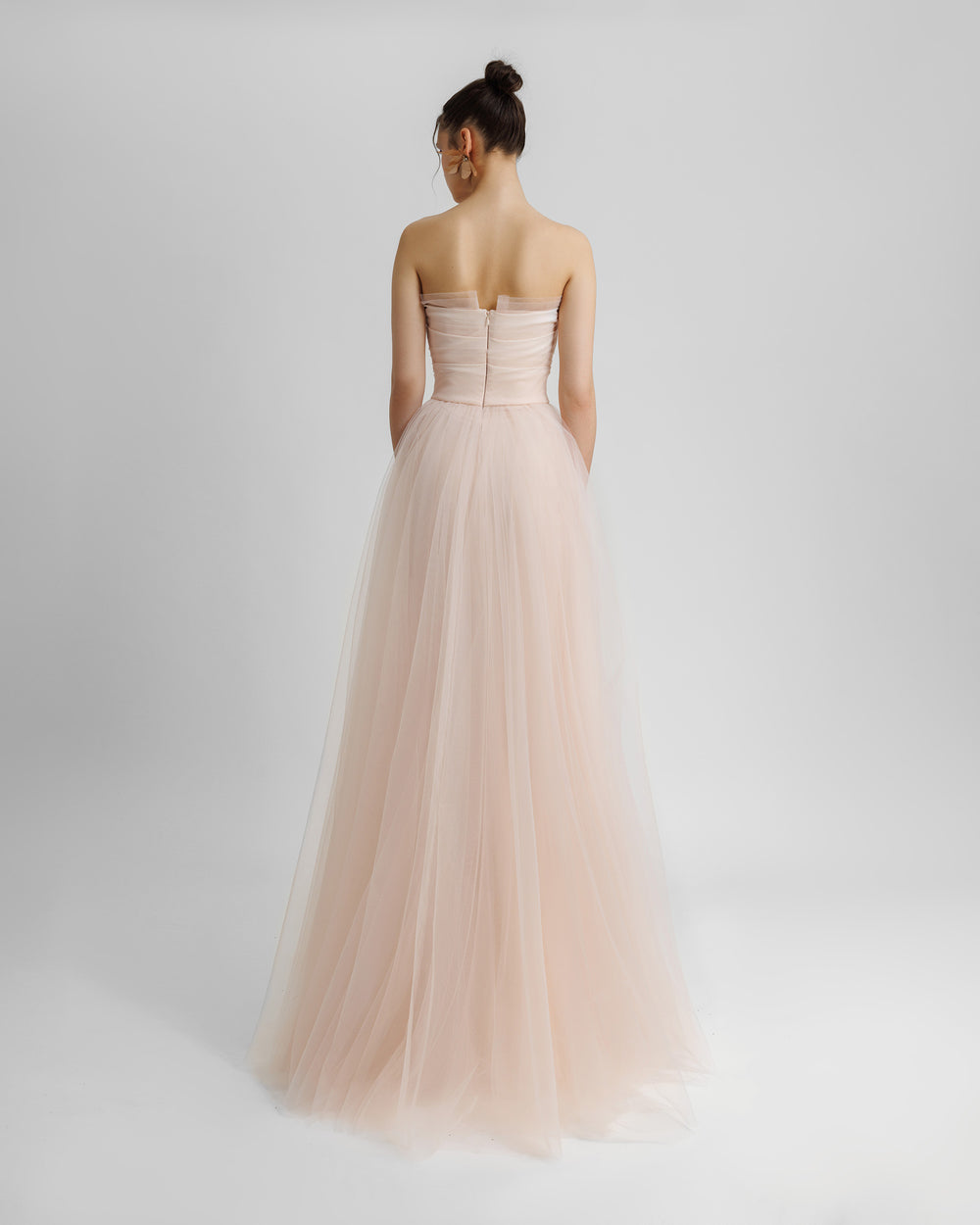 The back of a strapless, flared long blush evening dress with draping details on the bust line.