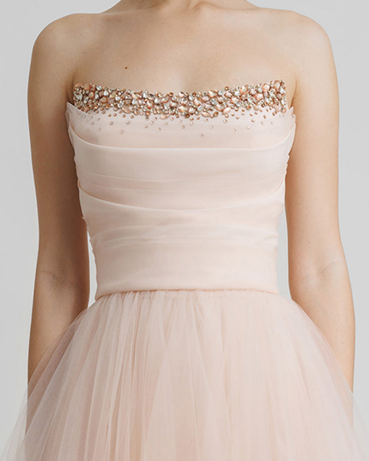 A close-up of a strapless, flared long blush evening dress with beading and draping details on the bust line.