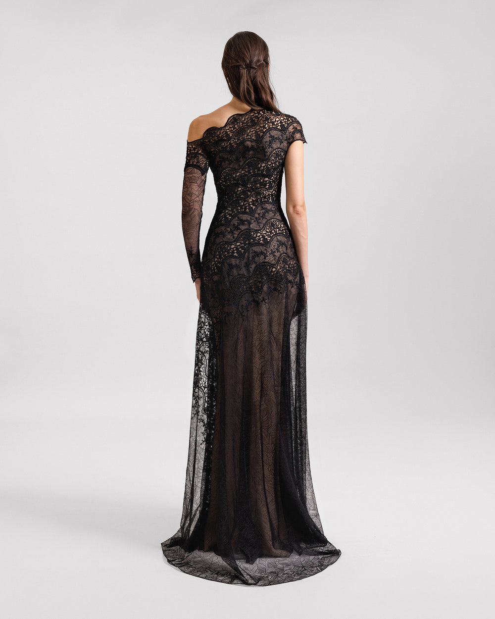 The back of an asymmetrical neckline black evening dress in embroidered lace featuring a one long sleeve.