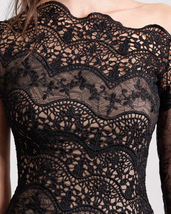 A close-up of an asymmetrical neckline black evening dress in embroidered lace featuring a one long sleeve.